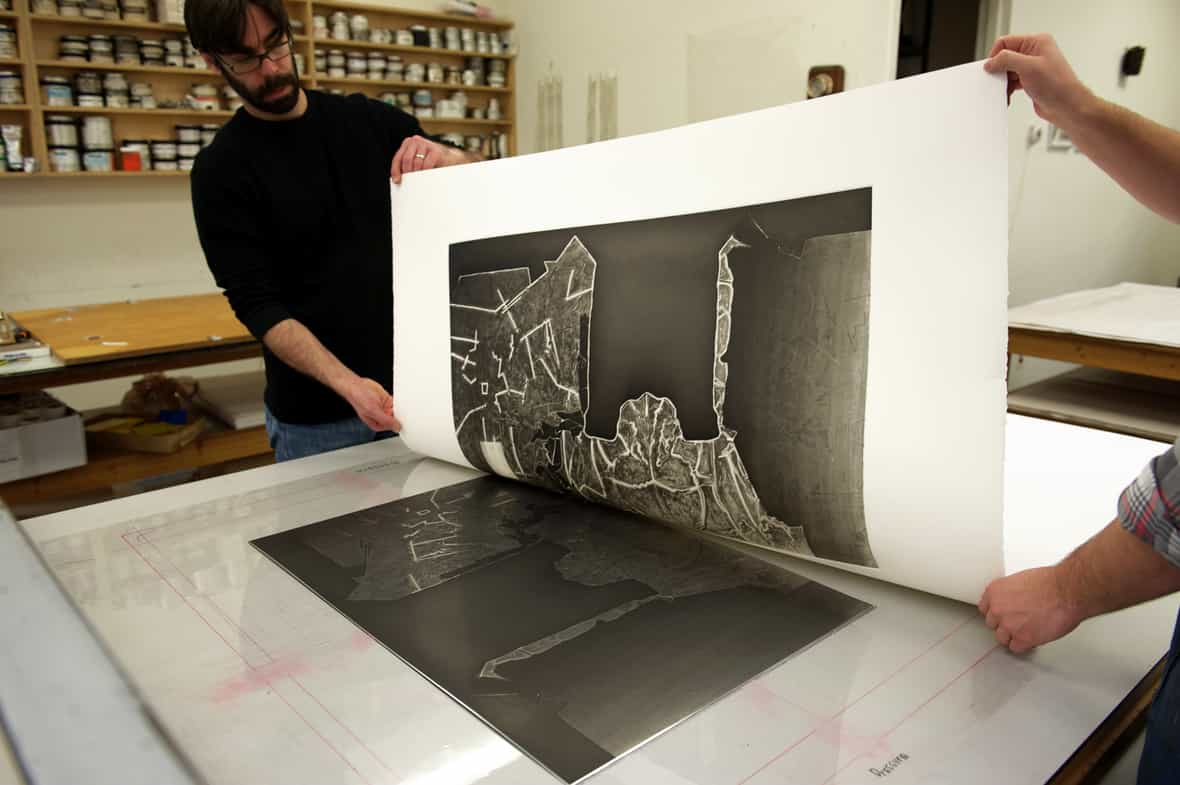 Printmakers Jason Miller and Steven Fournier pulling a print from an etching plate for Jasper Johns "Regrets."