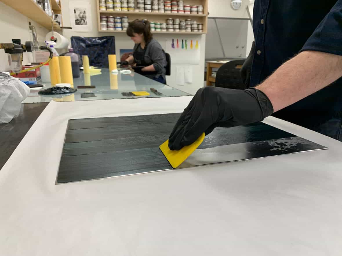 Printer Michael Rahn carding ink onto an etching plate.