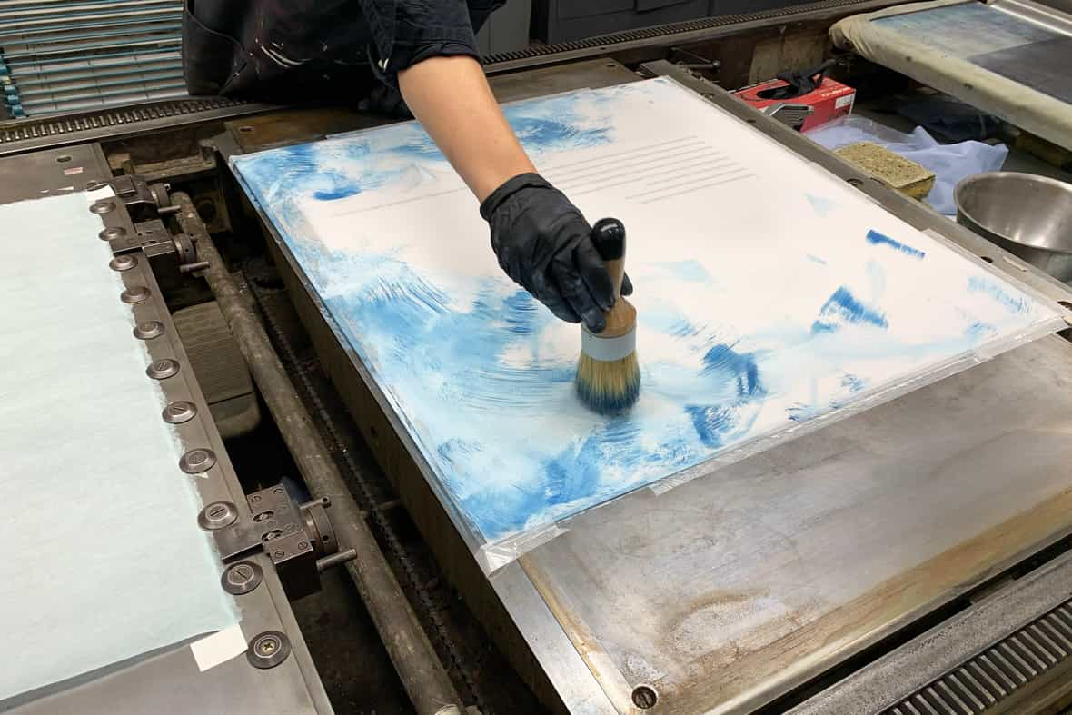 Artist Martha Tuttle applying ink with a round brush on a sheet of mylar to be printed on a lithography press.