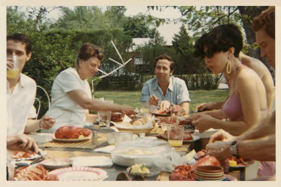 Tatyana Grosman, Robert Rauschenberg, and guests seated around the picnic table outside of Skidmore Place.
