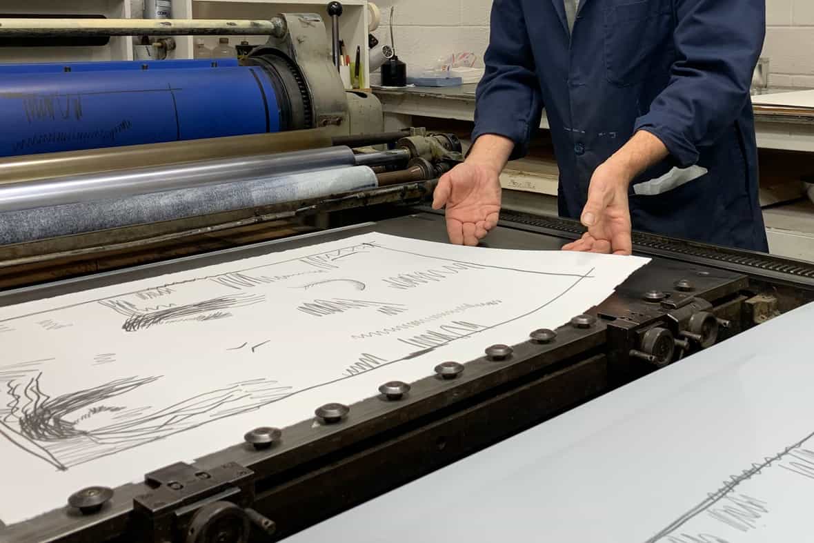 A man picking up a sheet of paper off the surface of an offset lithographic press.