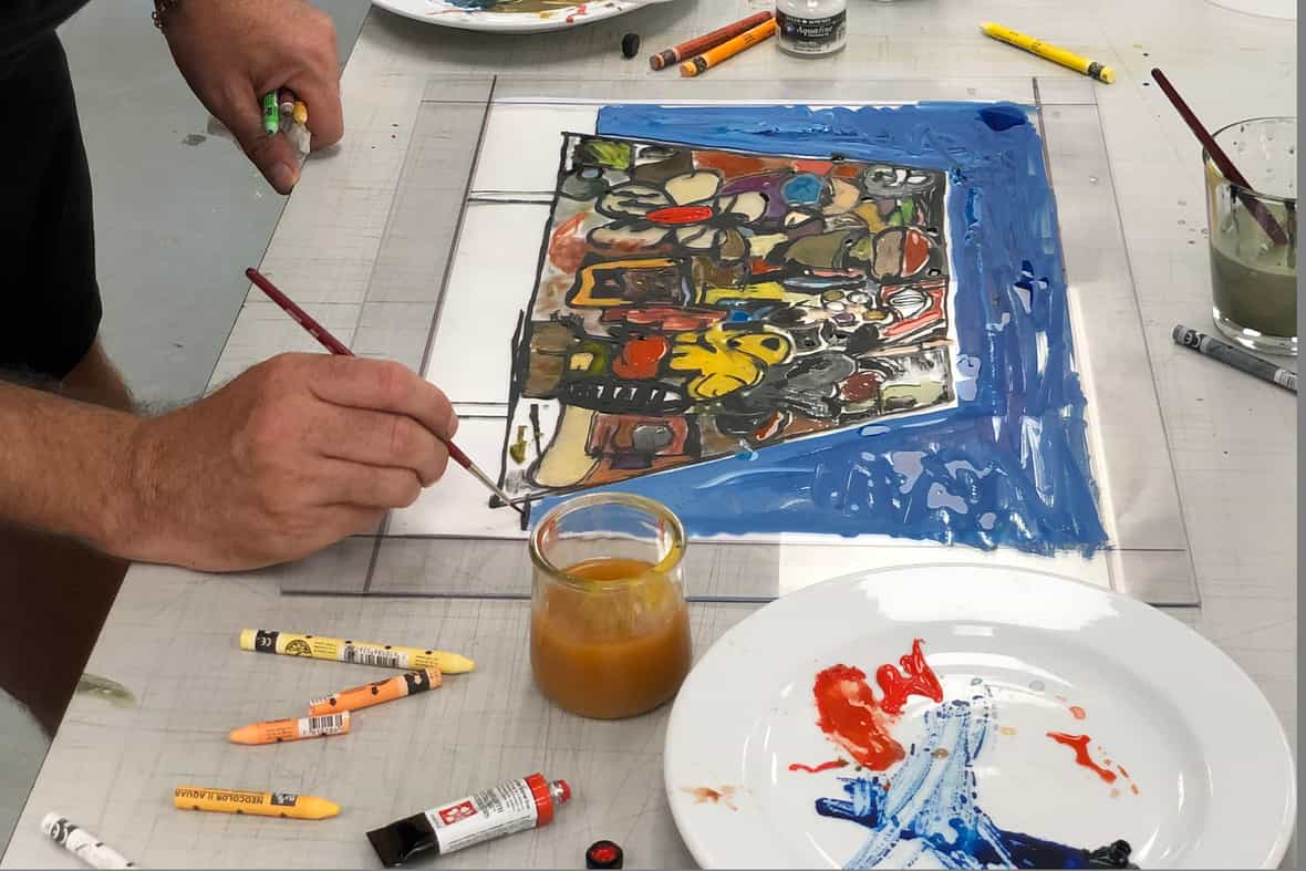 Artist Eddie Martinez standing over a table while painting with a paintbrush on the surface of a clear plexi plate.