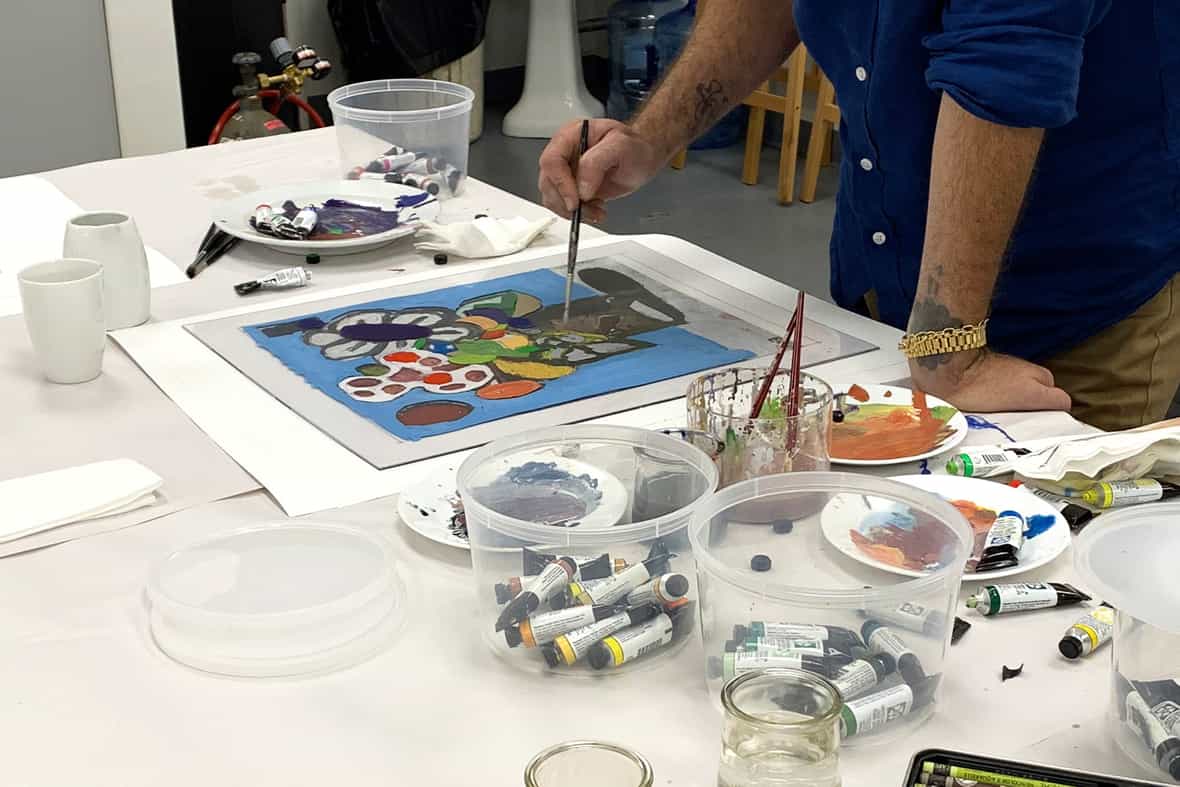 Artist Eddie Martinez standing over a table while painting with a paintbrush on the surface of a clear plexi plate.