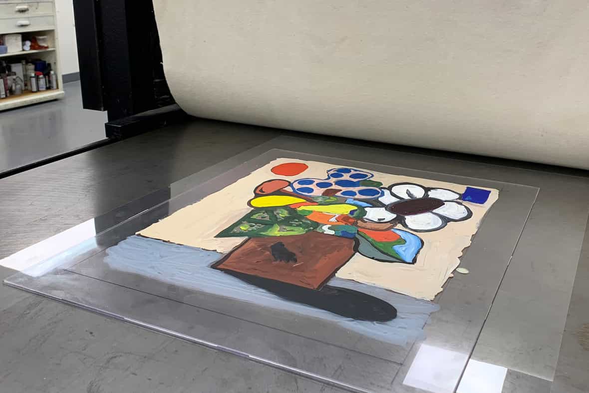 Close up image of a plexiglass plate on the bed of an etching press, an image painted in watercolor on the surface of the plexiglass.