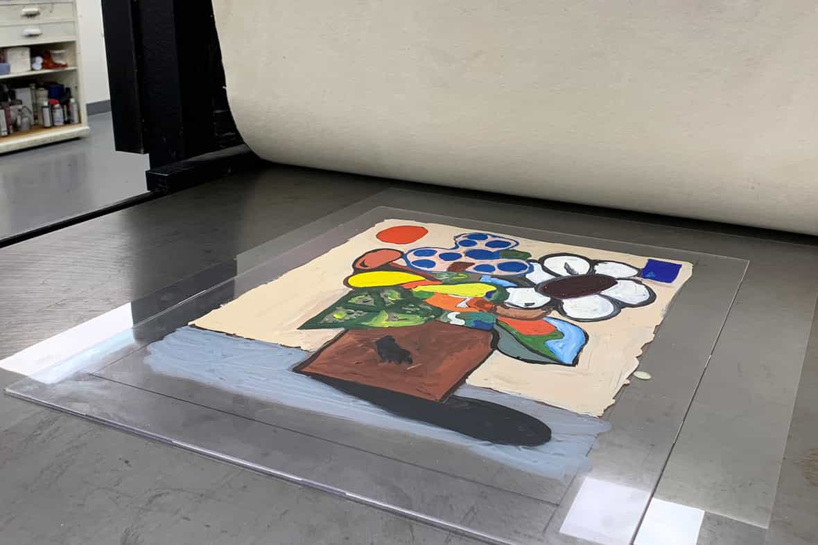 Close up image of a plexiglass plate on the bed of an etching press, an image painted in watercolor on the surface of the plexiglass.