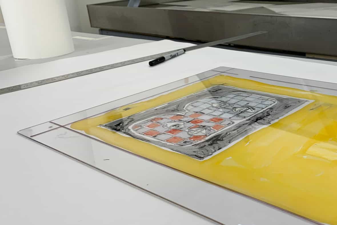 A clear plexiglass plate resting on a table after being printed through an etching press.