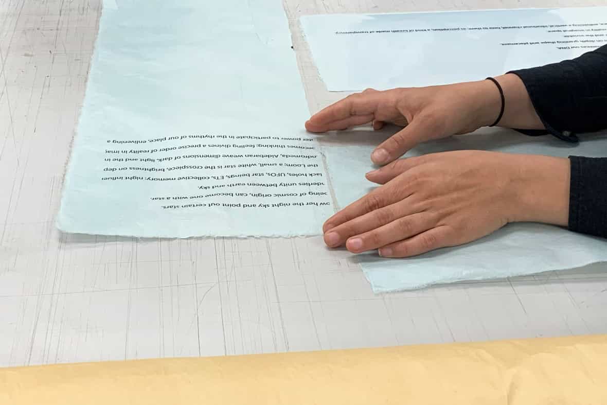 Artist Martha Tuttle's hands placing a poem on various papers.