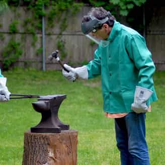 Richard Tuttle in the backyard pounding a raw ball of copper using a hammer, blowtorch, and an anvil.