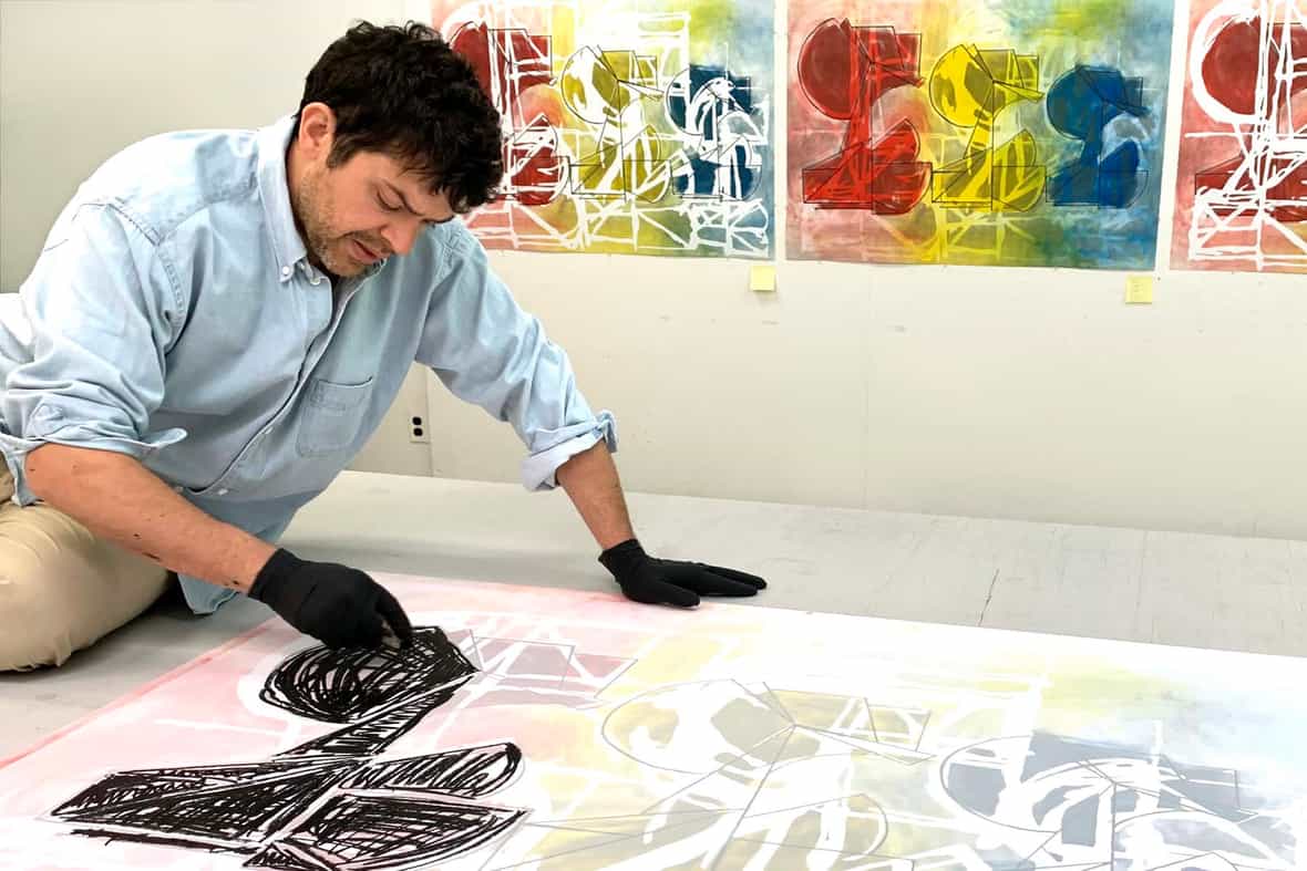 Wyatt Kahn sitting on a table, drawing on a mylar for a litho plate.