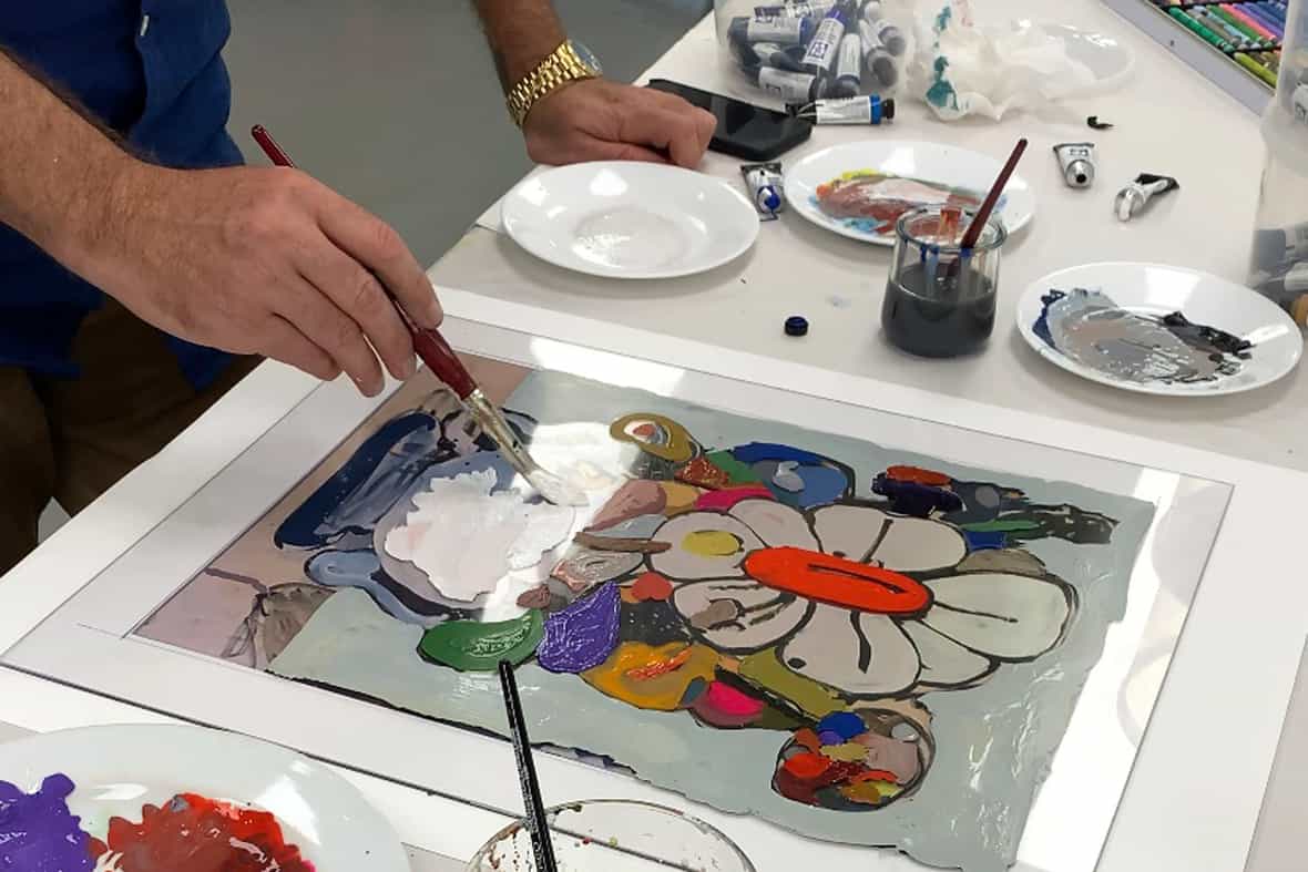 Artist Eddie Martinez standing over a table while painting with a paintbrush on the surface of a clear plexi plate.